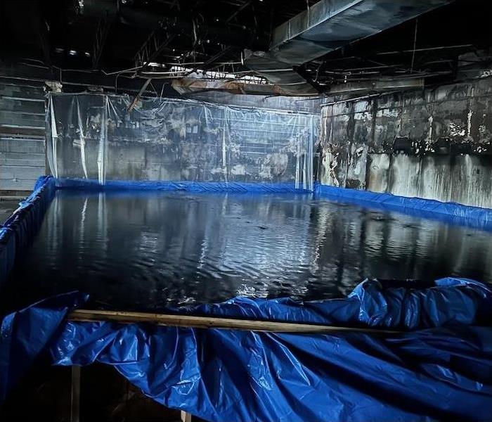 a blue tarp creating a pool in the basement of a manufacturing plant with fire damage on the walls