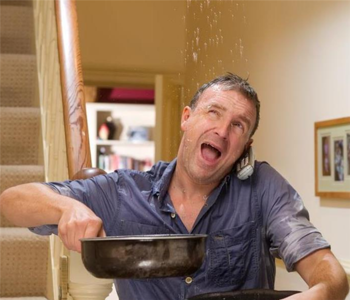 a man on the phone while holding pots and pans to catch the water falling from his ceiling