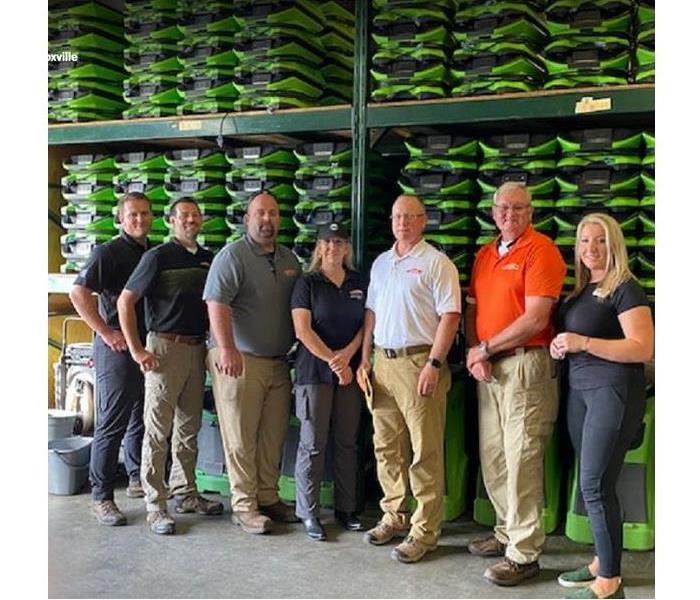 SERVPRO team members standing in front of stacked SERVPRO restoration equipment in a storage facility